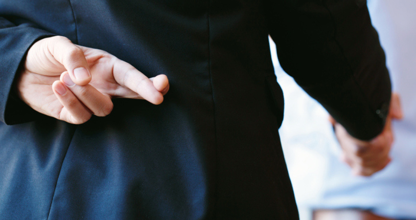 Man in dark suit with fingers crossed behind his back