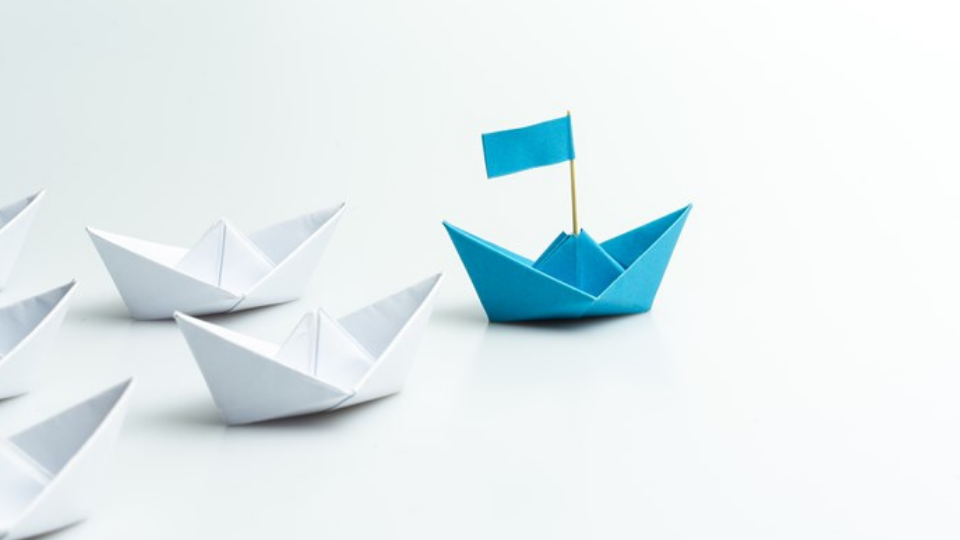 blue paper ship leading among white on white background
