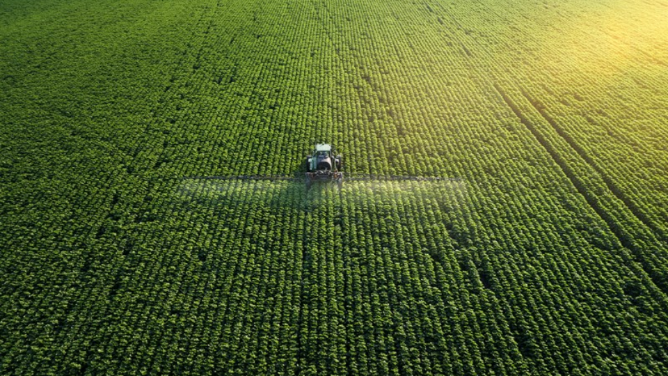 Taking care of the Crop. Aerial view of a Tractor fertilizing a cultivated agricultural field