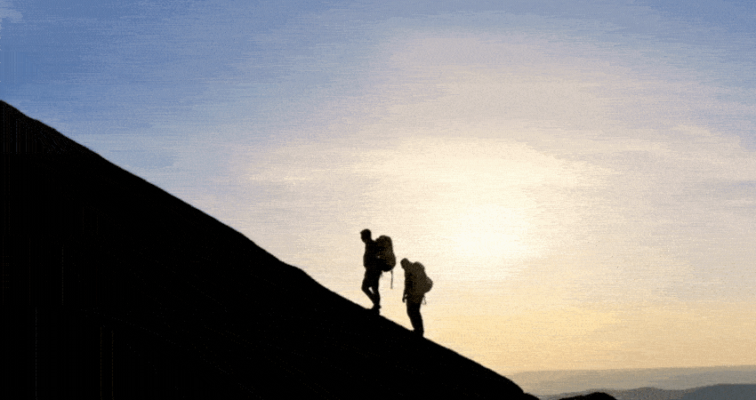 Silhouettes of a man and a woman with backpacks climbing to the top of the mountain