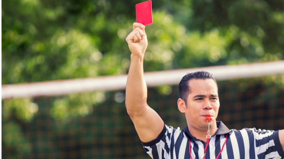 Hispanic soccer referee holds red card while blowing whistle